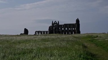 Whitby Abbey harabelerinin manzarası bulutlu gökyüzüne karşı tarihi bir dönüm noktası olan North York Moors Ulusal Parkı 'ndaki çimenli bir tepenin üzerinde duruyor.