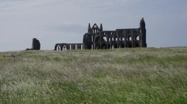 North York Moors Ulusal Parkı 'nda Whitby, İngiltere' de bulutlu bir gökyüzünün altında Whitby Abbey kalıntılarını gösteren manzara fotoğrafı.