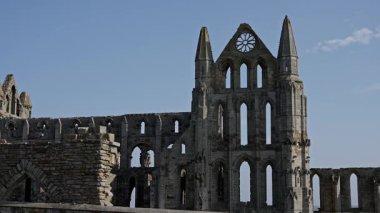 Whitby Abbey 'nin gotik kalıntıları, Kuzey York Moors Ulusal Parkı' nda büyüleyici bir manzara olan açık mavi gökyüzüne karşı dimdik ayakta duruyor.