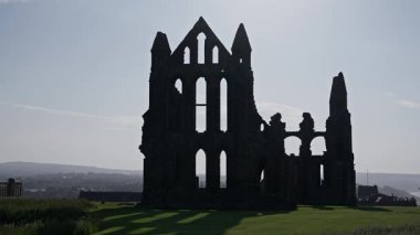Backlit Whitby Abbey harabeleri açık bir gökyüzüne karşı dimdik duruyor, Kuzey York Moors Ulusal Parkı 'ndaki tarih ve mimarinin özünü yakalıyor.