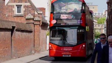 CAMBRIDGE, İngiltere - 11 Haziran 2025 - Cambridge, İngiltere 'de dar bir sokakta turistlerin yanından geçen kırmızı çift katlı gezi otobüsü