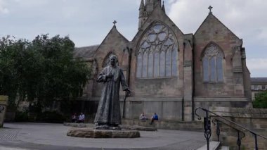 NEWCASTLE, İngiltere - 13 Haziran 2025 - İngiltere Newcastle 'daki St. Andrew Kilisesi önünde kollarını açmış duran bir rahibin bronz heykeli