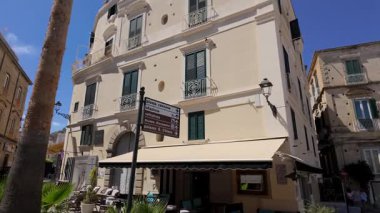 Tropea, Calabria 'daki pitoresk sokak manzarası, yön işaretleri olan bir bina, yerel gösterimler ve ulaşım seçenekleri sunuyor