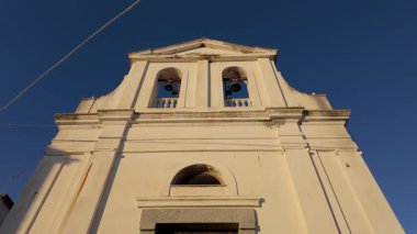 Güney İtalya, Calabria 'da açık mavi gökyüzüne karşı çan kulesiyle bembeyaz bir kilise cephesinin alçak açılı görüntüsü