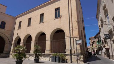 TROPEA, İTALYA - 2 Haziran 2025 - Tropea, Calabria, Güney İtalya 'da, dar bir sokakta turistlerin yürüdüğü saksılarda kemer ve bitkilerin bulunduğu eski bir binanın mimari görünümü