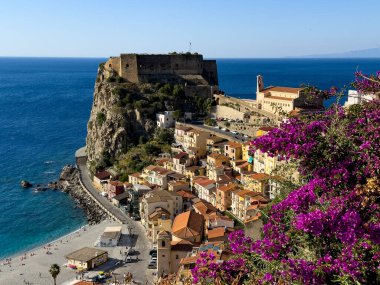 Renkli evler, kumsal, turkuaz deniz ve Ruffo Kalesi 'nin arka planında mor begonvil çiçekleri olan Scilla' nın panoramik manzarası.
