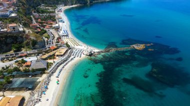 Tropea 'nın kıyı şeridinin nefes kesici manzarası kristal berrak turkuaz suları, plaj şemsiyeleri ve kayalık bir çıkıntısı var.