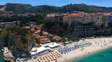 Renkli plaj şemsiyeleri, turkuaz kristal deniz, evler ve yaz tatili boyunca yeşil tepelerle Tropea, Calabria 'nın hava manzarası