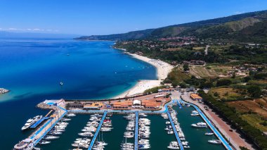Güney İtalya, Calabria 'da, yaz güneşinin altında turkuvaz suları ve beyaz kumlu Tropea limanı ve plajı havadan izleniyor.