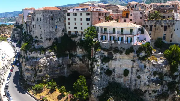 Uçurum kenarındaki binalar ve dolambaçlı kıyı yolu güneşli bir yaz gününde İtalya 'nın Tropea kentinin hava manzarasında gösteriliyor.
