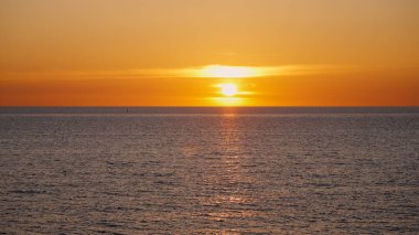 Sakin bir okyanusun üzerinde nefes kesici bir gün batımı alacakaranlık sırasında sıcak renklerle büyülü bir atmosfer yaratıyor.