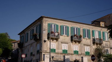 Vibo Valentia, Calabria, İtalya 'da yeşil kepenkleri ve çiçek saksılarıyla süslenmiş geleneksel İtalyan mimarisini sergileyen bir binanın yıpranmış dış cephesi