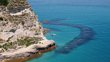 Turistler, Güney İtalya, Calabria 'daki Tropea plajının turkuaz sularında pedal teknesinde dinleniyor ve yüzüyorlar.
