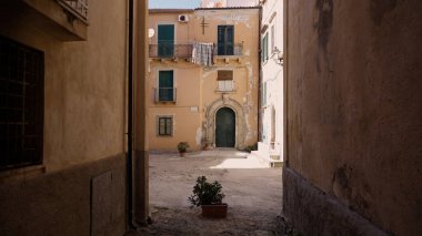 Tropea 'nın tarihsel cazibesini yakalayan yıpranmış binalar ve saksı bitkileriyle ıssız bir avluya açılan dar bir sokak.