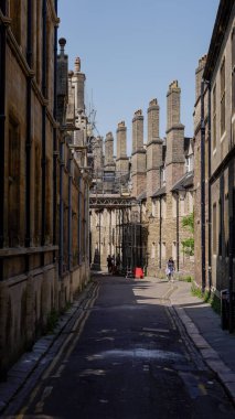 CAMBRIDGE, İngiltere - 11 Haziran 2025 - Güneşli bir yaz gününde Cambridge, İngiltere 'de dar bir sokakta iskele ve bacalarla yürüyen turistler