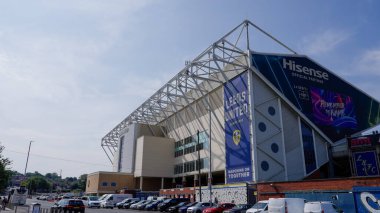 LEEDS, İngiltere - 11 Haziran 2025 - Leeds, İngiltere 'deki Elland Road Stadyumu, Leeds United Futbol Kulübü' nün evi, güneşli bir günde reklam pankartları ve park edilmiş araçlar sergileniyor.