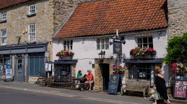 HELMSLEY, İngiltere - 12 Haziran 2025 - İnsanlar Kuzey Yorkshire 'da büyüleyici bir pazar kasabası olan Helmsley' deki geleneksel bir barın dışında yaz gününün tadını çıkarıyorlar