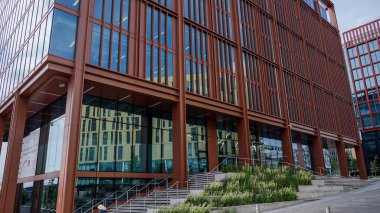 NEWCASTLE, İngiltere - 13 Haziran 2025 - Çarpıcı kırmızı çelik ve cam cepheli modern ofis binası, Newcastle 'daki kentsel manzarayı Tyne üzerine yansıtıyor