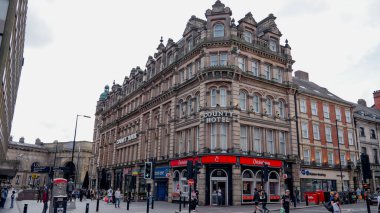 NEWCASTLE, UK - 13 Haziran 2025 - İngiltere 'nin Newcastle şehrinde tarihi bir bina, arkasında dükkanlar, restoranlar ve Newcastle Merkez İstasyonu var