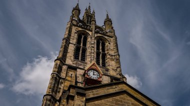 Aziz Niklas Katedrali 'nin görkemli kulesinin alçak açılı görüntüsü ve dinamik bulutların arka planına karşı saat