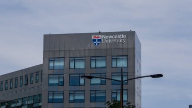 NEWCASTLE, İngiltere - 13 Haziran 2025 - Newcastle Üniversitesi 'nin modern binası ön cephesinde logosu görünür, bulutlu bir gökyüzünün altında
