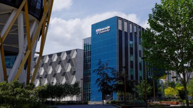 NEWCASTLE, İngiltere - 13 Haziran 2025 - Newcastle Üniversitesi 'nin modern binası Newcastle' da Tyne, İngiltere üzerinde bulutlu bir gökyüzünün altında fütürist bir binanın yanında yükseliyor
