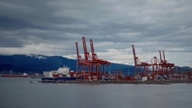 VANCOUVER, CANADA - 11 Nisan 2017 - Vancouver ticari limanındaki yük konteynerleri ve bulutlu bir gökyüzünün altında Seymour Dağı