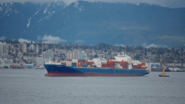 VANCOUVER, CANADA - 11 Nisan 2017 - Vancouver limanında destek ve karlı dağlar ve arka planda şehir manzarası olan büyük konteyner gemisi