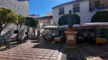Marbella, İspanya 'daki San Bernabe Meydanı' ndaki San Bernabe heykelini çevreleyen açık hava restoran masaları ve bankları - MARBELLA, İspanya - 30 Mart 2025