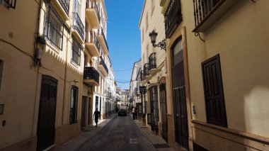İspanya 'nın Ronda şehrinde balkonları, dükkanları ve açık mavi gökyüzü olan dar bir caddeyi tanımlayan geleneksel mimari - RONDA, SPAIN - 28 Mart 2025