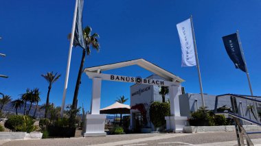 Banus Sahili 'nin beyaz girişi, rüzgarda dalgalanan bayraklar, Marbella, İspanya' da turistleri karşılama - MARBELLA, İspanya - 30 Mart 2025