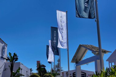 Marbella, İspanya 'da rüzgarda dalgalanan Banos Beach logosu olan beyaz ve koyu dikey bayraklar - MARBELLA, İspanya - 30 Mart 2025