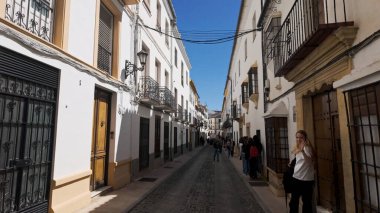 İspanya 'nın Ronda şehrinde beyazlatılmış binalar ve balkonlarla kaplı dar kaldırım taşlarını araştıran turistler - RONDA, SPAIN - 28 Mart 2025