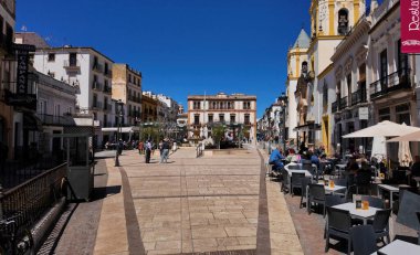 İnsanlar, Ronda, İspanya 'nın ana meydanı olan Plaza del Socorro' da güneşli bir günün tadını çıkarıyorlar. Restoranları ve kiliseleri olan RONDA, SPAIN - 28 Mart 2025