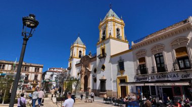 Güneşli günün tadını çıkaran turistler Plaza de la Merced ve Ronda, İspanya 'daki Santa Maria Belediye Başkanı Kilisesi - RONDA, İspanya - 28 Mart 2025