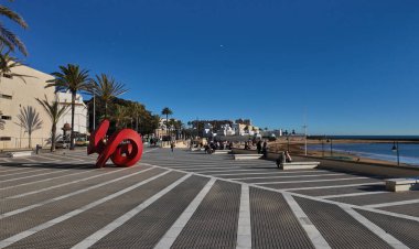 Cadiz 'in modern kırmızı heykel, palmiye ağaçları ve arka planda plaj manzarası güneşli bir günde - CADIZ, SPAIN - 26 Mart 2025