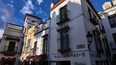 İspanya 'nın Sevilla şehrinde balkon ve dükkanlara sahip beyaz cepheler, açık mavi gökyüzü altında - SEVILLE, SPAIN - 25 Mart 2025