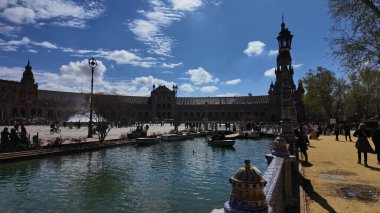 İspanya 'nın Sevilla kentindeki Plaza de Espana kanalının önünde küçük tekneler güneşli bahar gününde turistlerle birlikte yüzüyor - SEVILLE, SPAIN - 25 Mart 2025