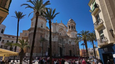 Plaza de la Katedral 'de güneşli bir günün keyfini çıkaran turistler Cadiz, İspanya' daki görkemli Cadiz Katedrali ve palmiye ağaçları - CADIZ, İspanya - 26 Mart 2025