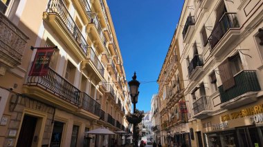 İspanya 'nın Cadiz kentinde dar bir caddeyi karakterize eden geleneksel mimari, balkonlar, bir sokak lambası ve açık mavi gökyüzü - CADIZ, SPAIN - 26 Mart 2025