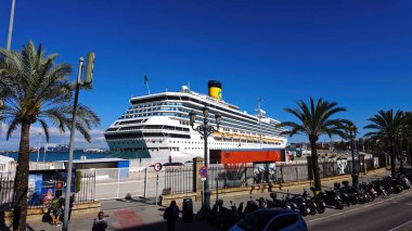 İspanya 'nın Cadiz kentinde demirli bir yolcu gemisi, parlak güneşli bir günde palmiye ağaçları ve park etmiş scooterlarla çevrili - CADIZ, SPAIN - 26 Mart 2025