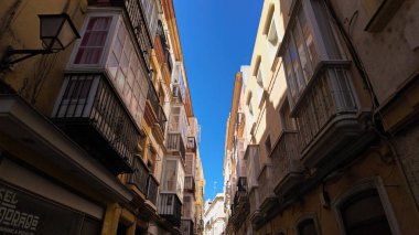 İspanya 'nın Cadiz kentindeki resmi dar bir caddenin düşük açılı görüntüsü, binalara geleneksel koyu pencereler ve açık mavi gökyüzü - CADIZ, SPAIN - 26 Mart 2025