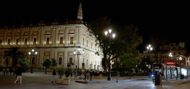 Seville 'in San Telmo Sarayı, modern bir tramvayın geçmesiyle gece aydınlandı, tarih ve modernite arasında bir zıtlık yarattı - SEVILLE, SPAIN - 25 Mart 2025