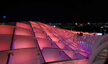 Metropol Şemsiyesi 'nin çatı geçidinde yürüyen turistler gece Sevilla, İspanya' da pembe ve mor ışıklarla aydınlatılıyor - SEVILLE, İspanya - 25 Mart 2025