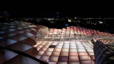 Metropol Şemsiyesi 'nin yükseltilmiş geçidinde gece renkli ışıklar ve arka planda Sevilla silueti - SEVILLE, SPAIN - 25 Mart 2025
