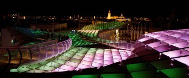 Metropol Şemsiyesi 'nin modern ahşap yapısı ve gece Sevilla şehir manzarasını aydınlatan renkli ışıklar - SEVILLE, SPAIN - 25 Mart 2025