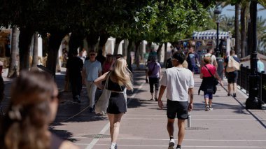 İspanya 'da popüler bir turizm beldesi olan Marbella' daki ağaçlar ve dükkanlarla yayaların arasında gezinen insanlar - MARBELLA, SPAIN - 30 Mart 2025