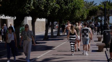 İnsanlar, ağaçlarla kaplı bir sahil boyunca geziniyor, yaz havasının tadını çıkarıyorlar - MARBELLA, SPAIN - 30 Mart 2025