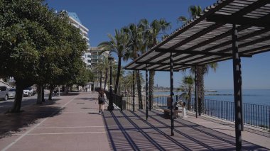 İspanya 'nın Marbella şehrinde güneşli bir günde palmiye ağaçlarının gölgesinde yürüyen kadın - MARBELLA, İspanya - 30 Mart 2025