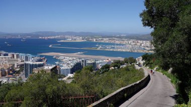 Güneşli bir günde manzaralı bir yolda yürüyen turistler, Cebelitarık Havalimanı, Algeciras Körfezi ve şehir - GIBRALTAR, İngiltere - 31 Mart 2025